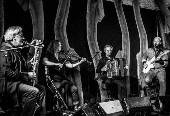 Quatre musiciens en concert dans une salle voûtée en pierre : saxophone, violon, accordéon et guitare électrique - Agrandir l'image, fenêtre modale