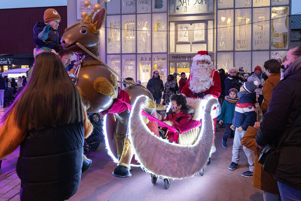 Père Noël en traîneau lumineux tiré par un renne géant, acclamé par des familles lors d'un spectacle de rue - Agrandir l'image, fenêtre modale