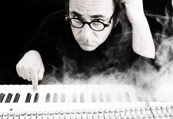 Patrick Ingueneau, regard intense et grimace expressive, effleure les touches d'un piano enveloppé de fumée - Agrandir l'image, fenêtre modale