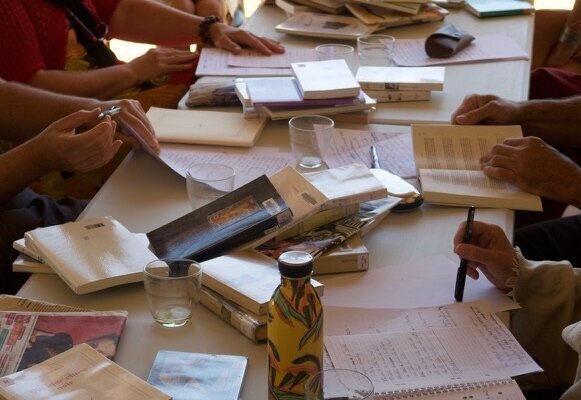 Groupe de participants assis autour d'une table garnie de livres ouverts, cahiers et feuilles manuscrites - Agrandir l'image, fenêtre modale