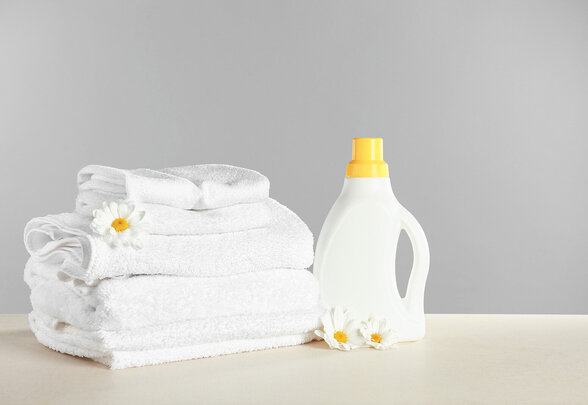 Serviettes blanches pliées et flacon de lessive à bouchon jaune, accompagnés de marguerites blanches - Agrandir l'image, fenêtre modale