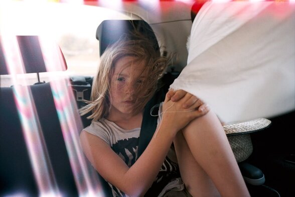 Enfant aux cheveux balayés par le vent, assis en siège auto, agrippant les genoux d'un adulte, avec reflets de voile argentique - Agrandir l'image, fenêtre modale