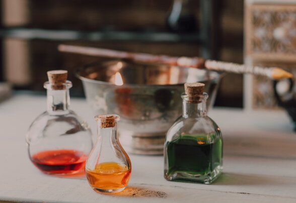Trois fioles en verre bouchées avec du liège contenant des liquides rouge, orange et vert, posées sur une table