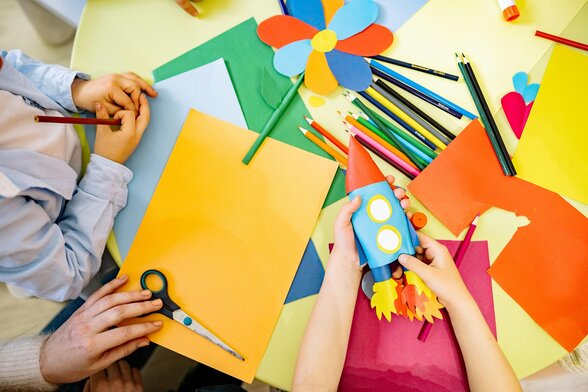 Mains créant une fusée en gobelet bleu et une fleur en papier coloré, crayons et ciseaux sur une table - Agrandir l'image, fenêtre modale