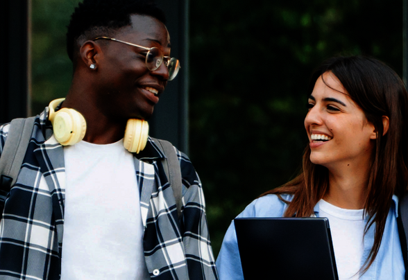 Deux étudiants souriants se font face devant le campus, l'un portant un casque audio, l'autre un ordinateur portable. - Agrandir l'image, fenêtre modale