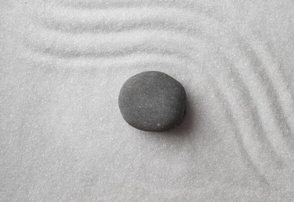 Galet gris poli sur du sable blanc finement ratissé, composition zen en résonance avec l'univers symbolique du spectacle - Agrandir l'image, fenêtre modale