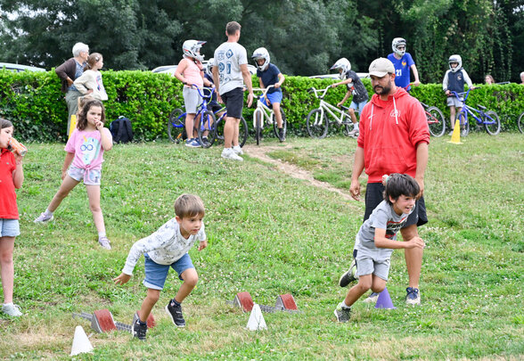 Groupe d'enfants courant entre des cônes de balisage sur l'herbe, encadrés par un animateur adulte. - Agrandir l'image, fenêtre modale