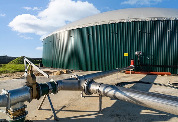 Digesteur anaérobie cylindrique vert avec coupole grise et canalisations métalliques sur site industriel extérieur - Agrandir l'image, fenêtre modale