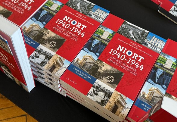 Plusieurs exemplaires de l'ouvrage disposés sur une table, couverture rouge illustrée de photographies d'archives de l'Occupation - Agrandir l'image, fenêtre modale