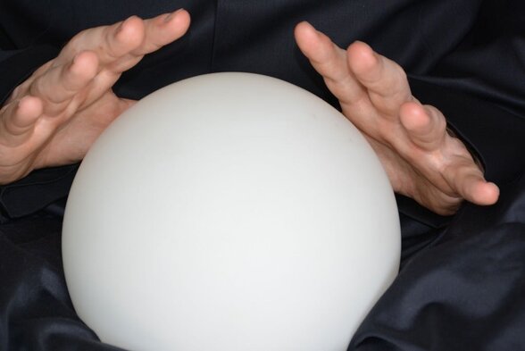 Mains aux doigts écartés survolant une boule de cristal blanche lumineuse posée sur tissu noir satiné - Agrandir l'image, fenêtre modale