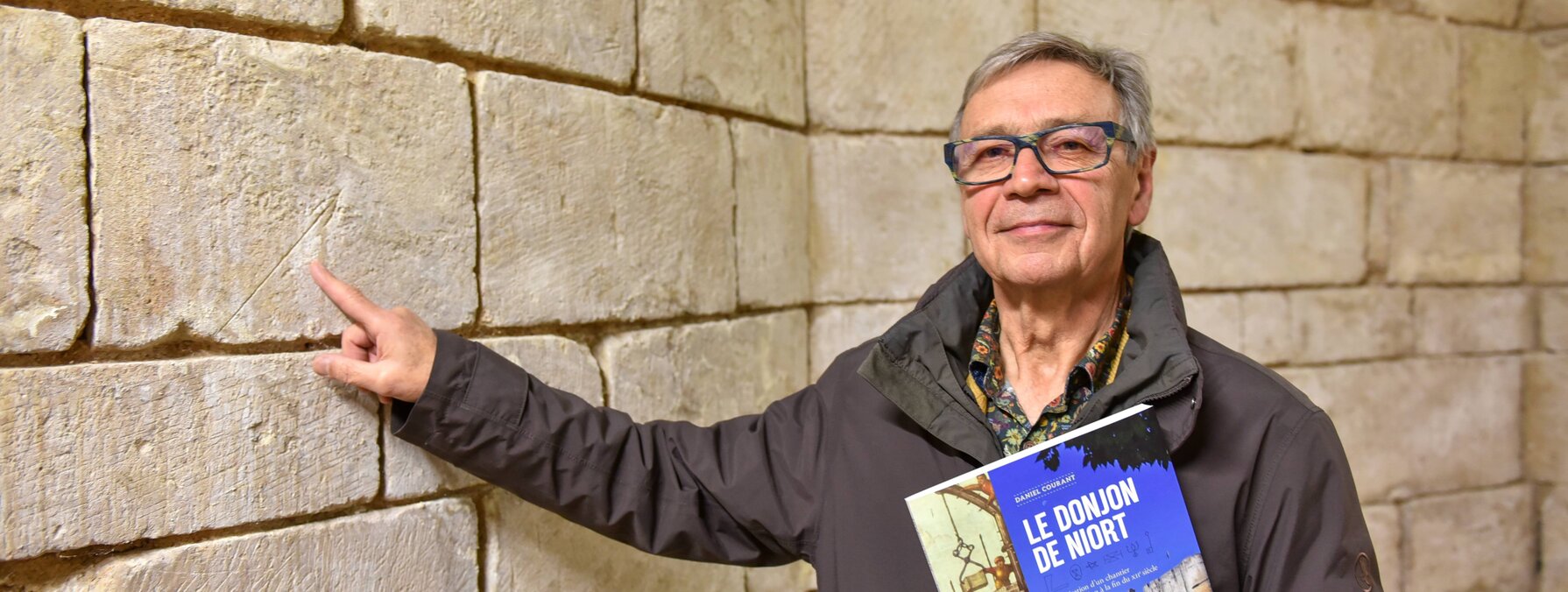 Daniel Courant, son livre à la main, montre une marque gravée dans la pierre