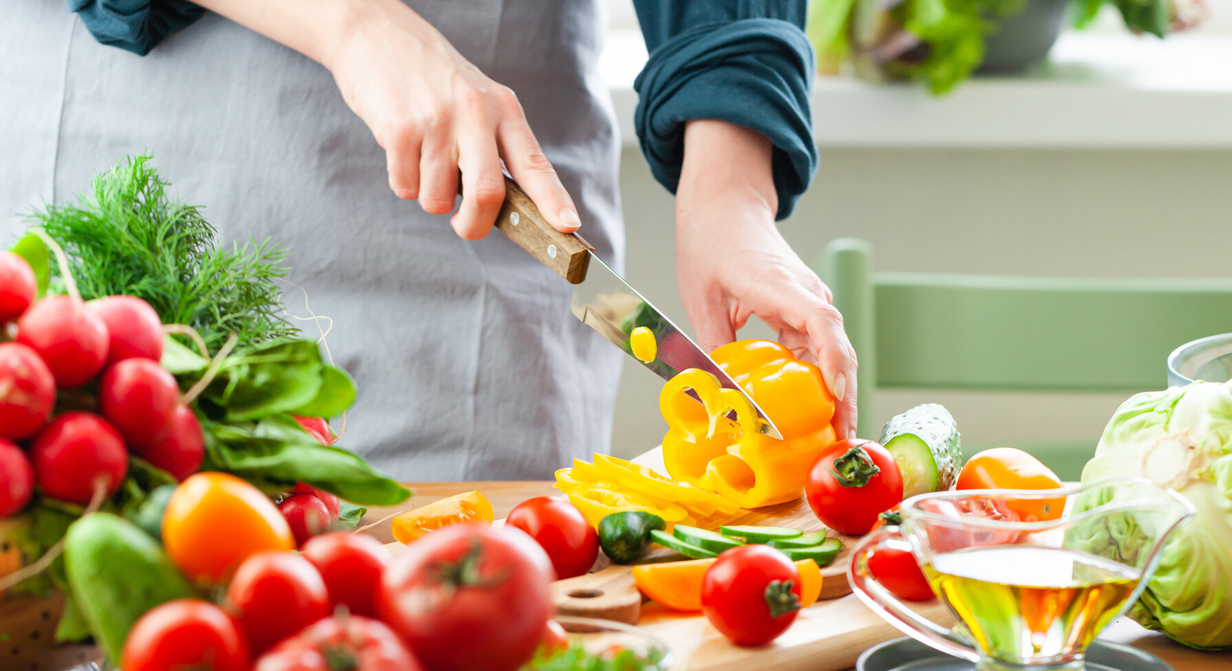 Personne découpant un poivron jaune entourée de légumes frais colorés sur un plan de travail de cuisine