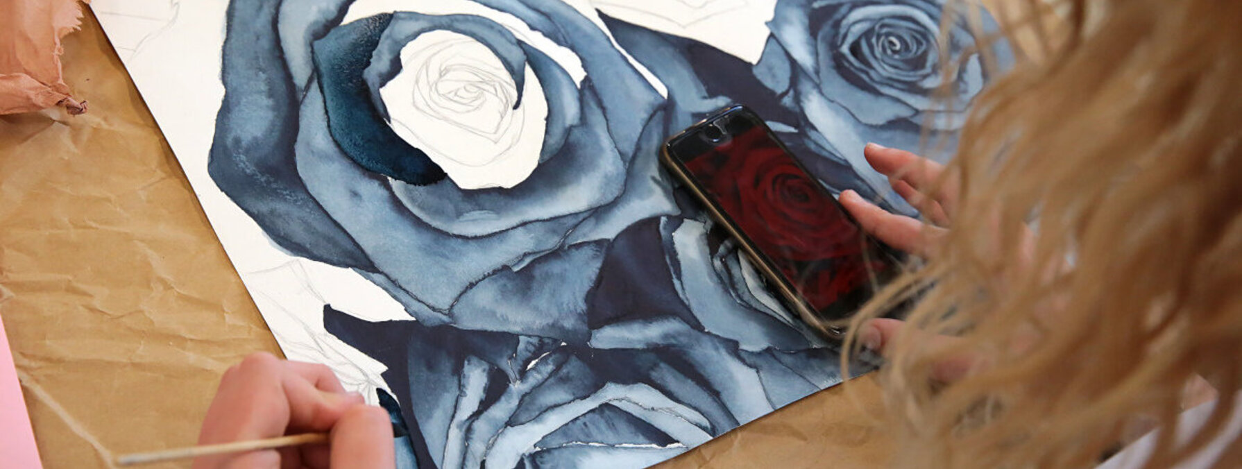 Élève réalisant une aquarelle de roses aux teintes bleues et grises, smartphone posé sur l'œuvre comme référence