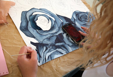 Élève réalisant une aquarelle de roses aux teintes bleues et grises, smartphone posé sur l'œuvre comme référence