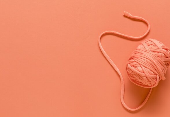 Pelote de fil rose saumon avec son extrémité déroulée, posée sur un fond de même teinte - Agrandir l'image, fenêtre modale