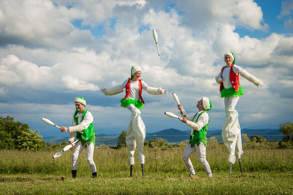 Quatre artistes costumés en lutins de Noël jonglent avec des massues blanches, deux d'entre eux sur échasses - Agrandir l'image, fenêtre modale