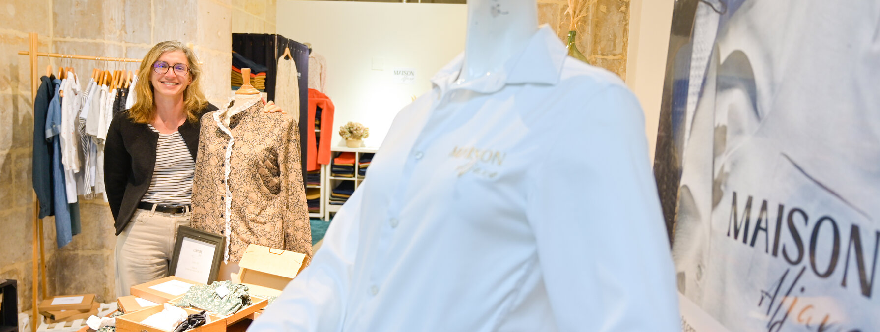 Sandrine Bertin souriante dans la boutique éphémère, avec un mannequin portant une chemise Maison Aljane au premier plan