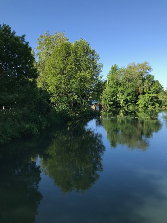 Berges arborées et végétation luxuriante se reflétant dans l'eau calme de la rivière, avec un pont en pierre en arrière-plan - Agrandir l'image, fenêtre modale