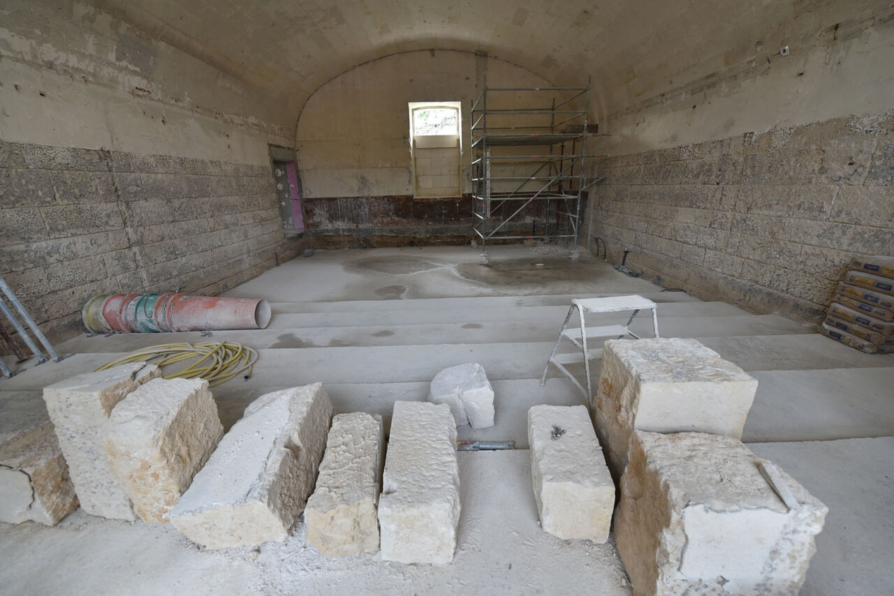 Chantier de rénovation intérieure : blocs de pierre de taille au sol, échafaudage, voûte en berceau et murs de moellon apparents