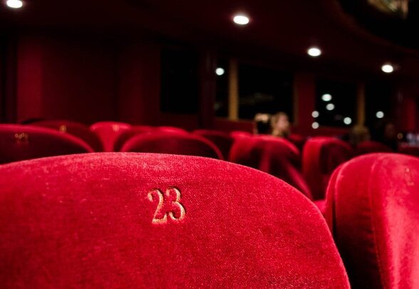 Rangées de fauteuils en velours rouge numérotés dans une salle de spectacle plongée dans la pénombre - Agrandir l'image, fenêtre modale