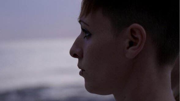 Jeune femme aux cheveux courts filmée de profil, regard tourné vers l'horizon, lumière crépusculaire sur fond de mer - Agrandir l'image, fenêtre modale