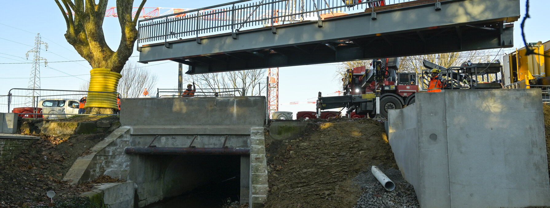 Grue de chantier soulevant la passerelle métallique au-dessus de la Romagne