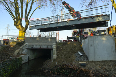 Grue de chantier soulevant la passerelle métallique au-dessus de la Romagne