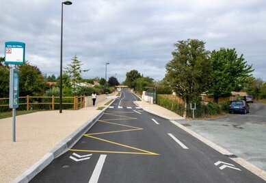 Voie cyclable aménagée avec marquage au sol jaune et blanc, séparée de la chaussée, longeant un arrêt de bus ligne 23