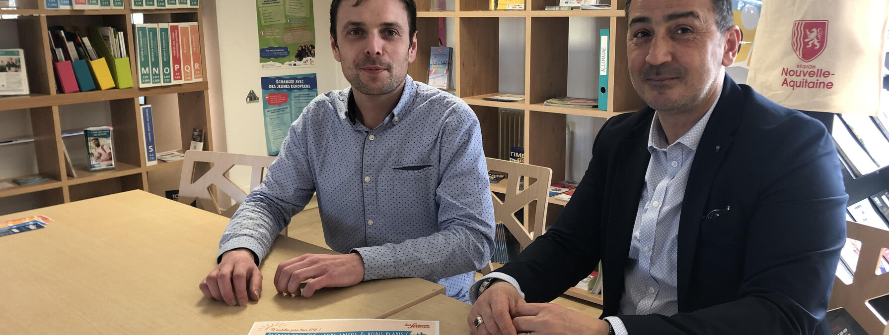 Deux représentants posent dans les locaux d'Info Jeunes Niort avec l'affiche du Forum des jobs d'été sur la table.