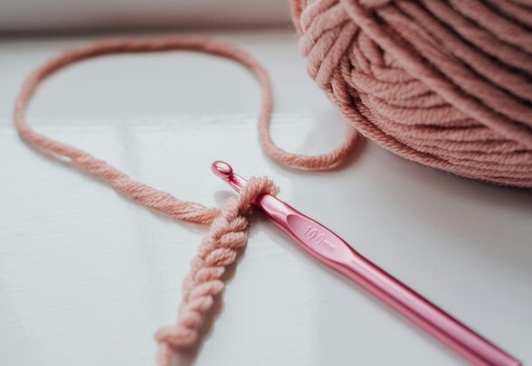 Un crochet rose métallique engagé dans une chaînette de mailles, posé près d'une pelote de fil vieux-rose - Agrandir l'image, fenêtre modale