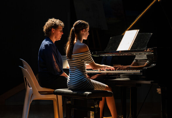 Une élève joue au piano à queue sous l'éclairage scénique d'une salle de concert, encadrée par une enseignante assise à ses côtés - Agrandir l'image, fenêtre modale