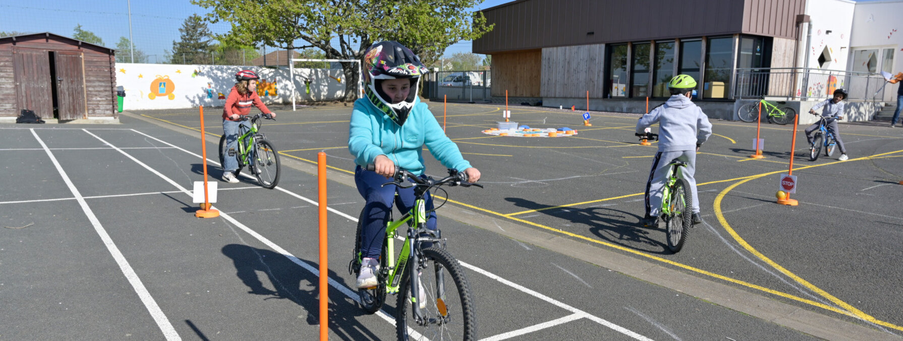 Enfants casqués manœuvrant à vélo sur un parcours balisé de cônes et marquages au sol dans une cour d'école