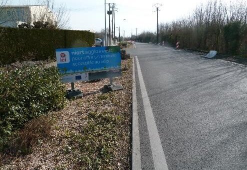 Panneau Niort Agglo « investit ici pour un territoire accessible au vélo » en bordure de route avec marquage cyclable au sol