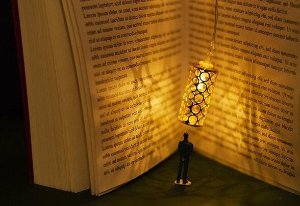 Personnage miniature debout dans un livre ouvert géant, éclairé par une lanterne suspendue, symbole de l'immersion dans la lecture - Agrandir l'image, fenêtre modale