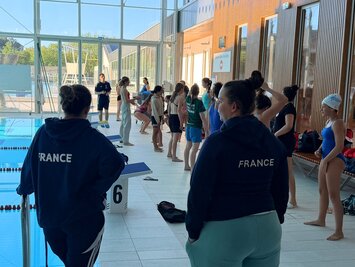 Joueuses alignées au bord du bassin intérieur, deux encadrantes en veste « FRANCE » dos à l'objectif