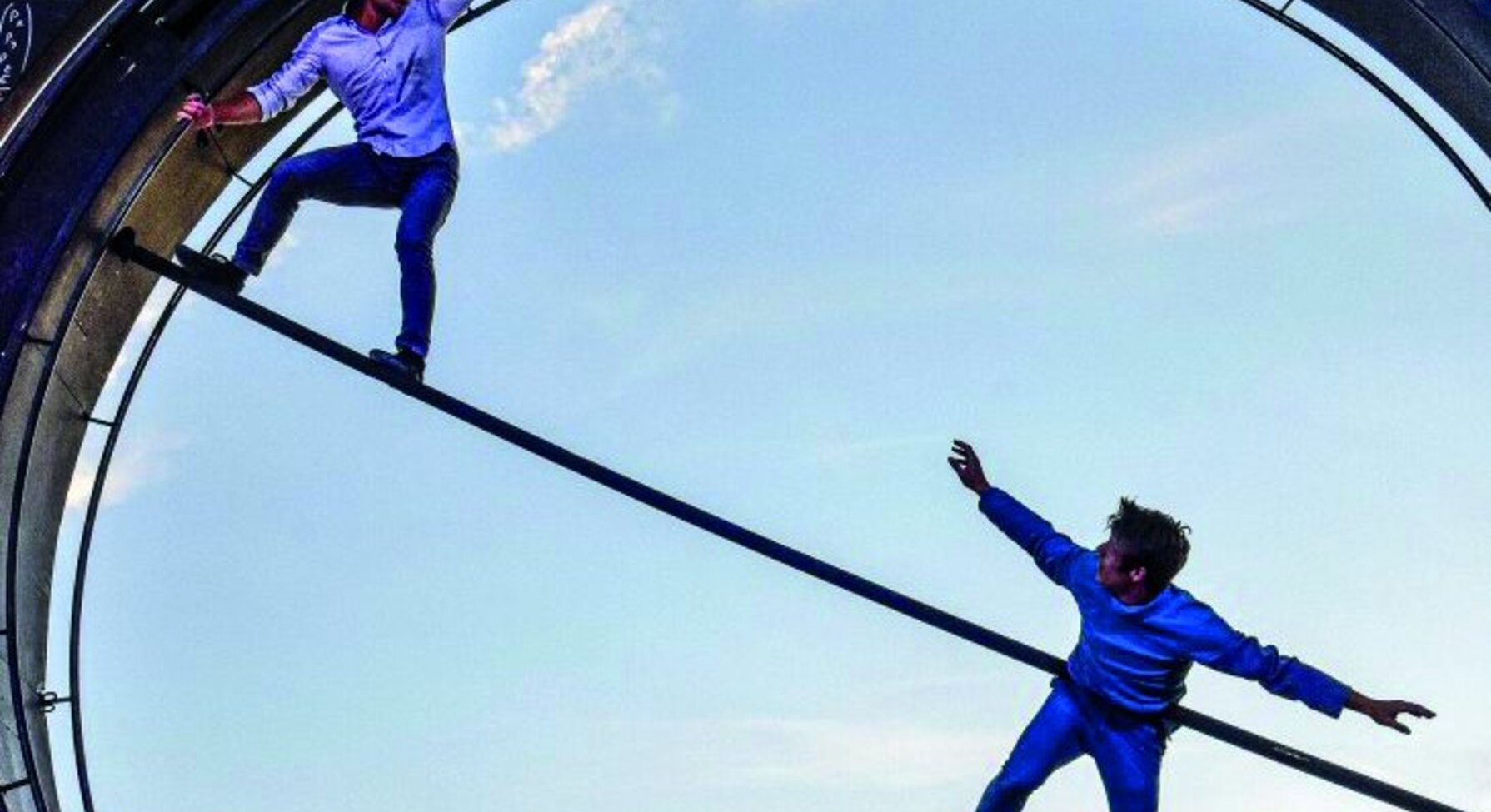 Deux interprètes dans l'Oculaire, grande roue couverte de formules mathématiques : l'un en équilibre sur une barre, l'autre suspendu dans les airs