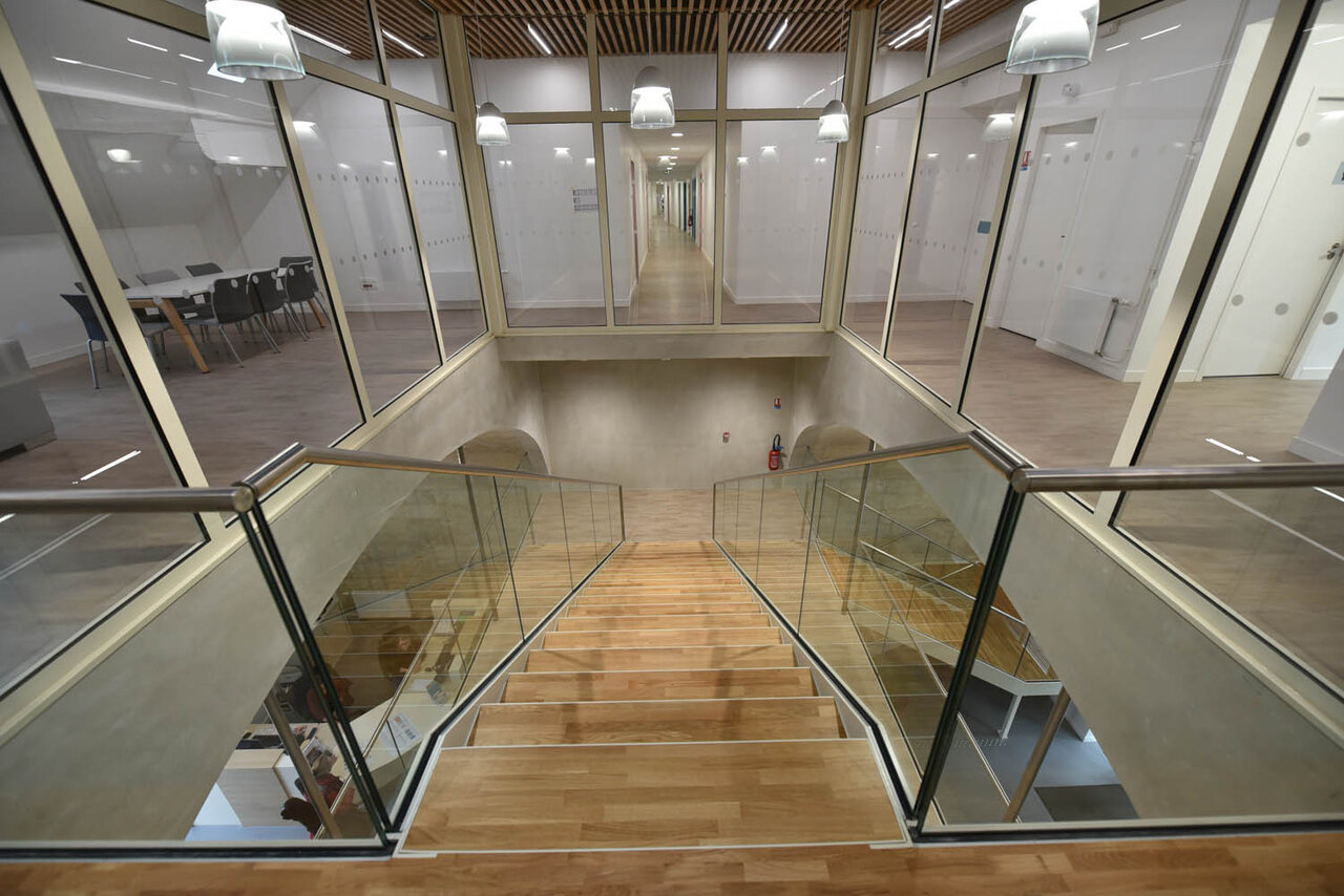 Hall intérieur avec escalier en bois à rampes vitrées, long couloir et salles de cours en enfilade