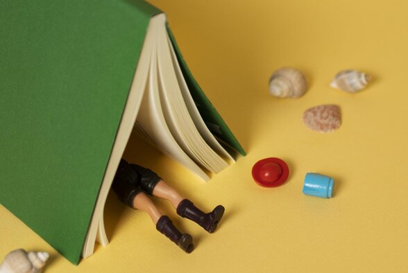 Livre ouvert en forme de tente abritant une figurine, entouré de coquillages et d'une mer en papier découpé sur fond jaune - Agrandir l'image, fenêtre modale