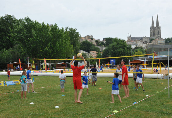 Jeunes joueurs de volley-ball sur gazon lors de Niort Plage, avec la cathédrale de Niort en arrière-plan - Agrandir l'image, fenêtre modale