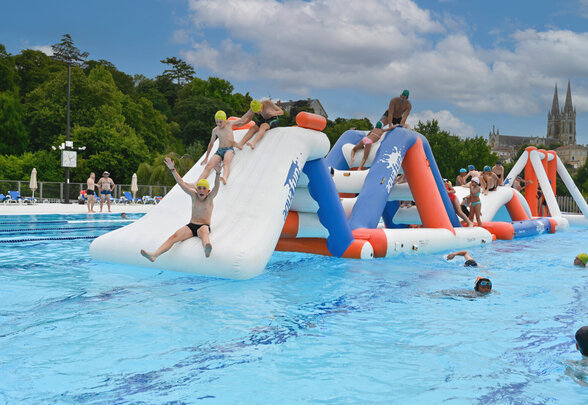 Enfants grimpant et glissant sur le parcours gonflable dans le bassin extérieur de la piscine - Agrandir l'image, fenêtre modale
