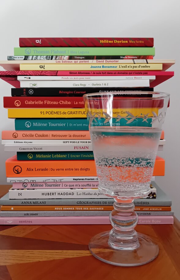 Pile de recueils de poésie contemporaine avec un verre d'eau pétillante posé devant, sur une table en bois