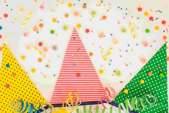 Triangles en papier à rayures rouges et pois jaunes et verts, parsemés de confettis et serpentins multicolores sur fond blanc. - Agrandir l'image, fenêtre modale