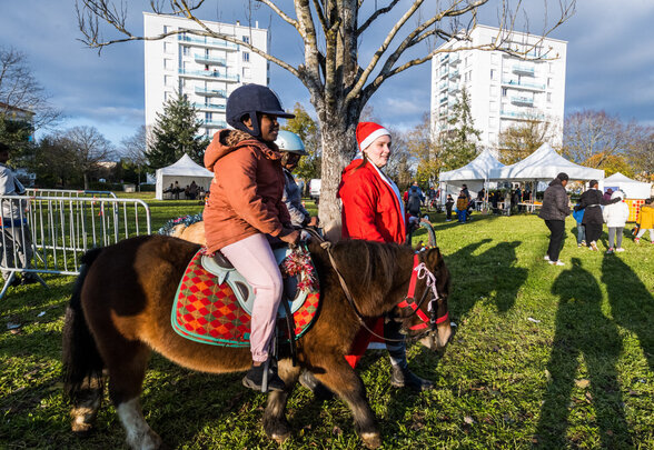 Enfant à dos de poney guidé par un animateur en costume de Père Noël lors des animations place Louis Jouvet - Agrandir l'image, fenêtre modale