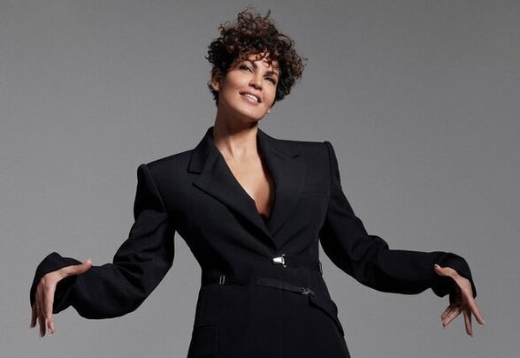 Nawell Madani, humoriste et comédienne, en pose expressive bras grands ouverts, regard tourné vers le haut - Agrandir l'image, fenêtre modale