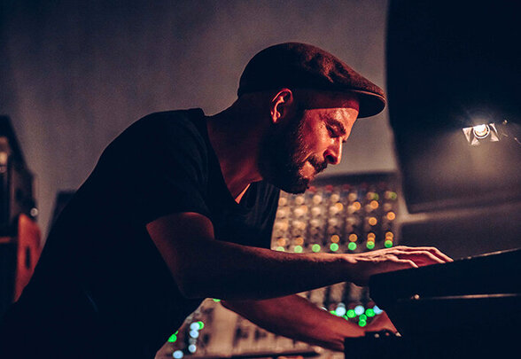 Nils Frahm penché sur ses claviers en concert, entouré de machines aux lumières colorées dans une salle sombre. - Agrandir l'image, fenêtre modale