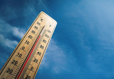 Thermomètre en bois affichant plus de 33 °C sur fond de ciel bleu, évoquant une vague de chaleur