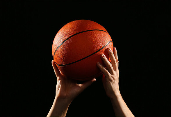 Un ballon de basketball orange saisi à deux mains levées, mis en lumière sur fond entièrement noir - Agrandir l'image, fenêtre modale