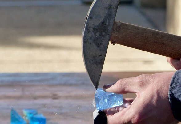 Mains fracturant un morceau de verre épais bleu translucide à l'aide d'un marteau de vitrailliste - Agrandir l'image, fenêtre modale
