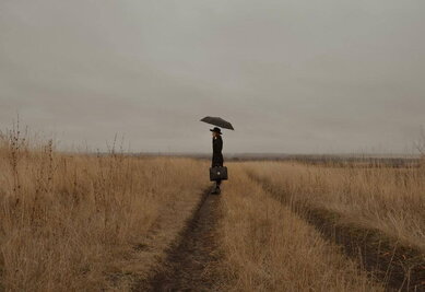 Concours de nouvelles des médiathèques une femme dans un champ. Elle s'abrite sous un parapluie et tient une sacoche à la main.