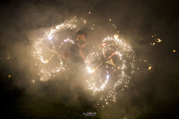 Un artiste manipule des engins pyrotechniques traçant des cercles d'étincelles lumineuses dans un nuage de fumée nocturne